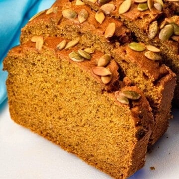 Moist slice of vegan pumpkin bread with pumpkin seeds on top.