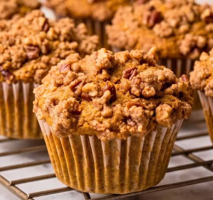A batch of baked vegan pumpkin muffins with pecan streusel on a cooling rack.