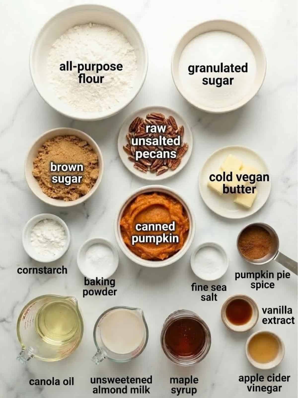 A selection of baking ingredients including flour, sugar, oil, almond milk, baking powder, vegan butter, and canned pumpkin.