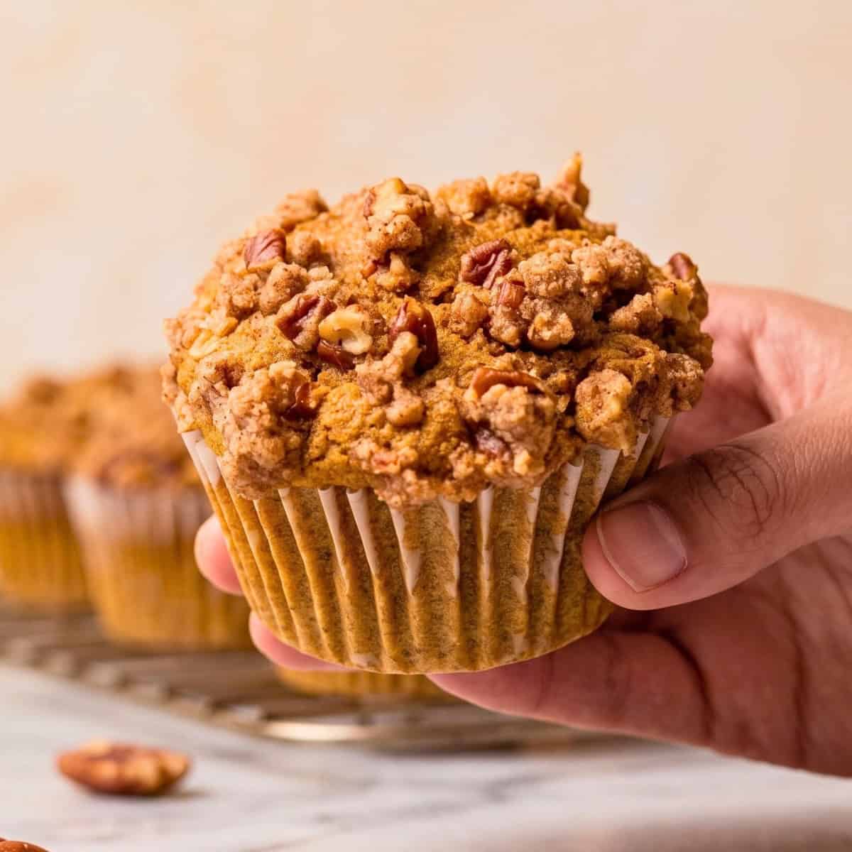 Someone holding up one baked vegan pumpkin muffin with pecan streusel.