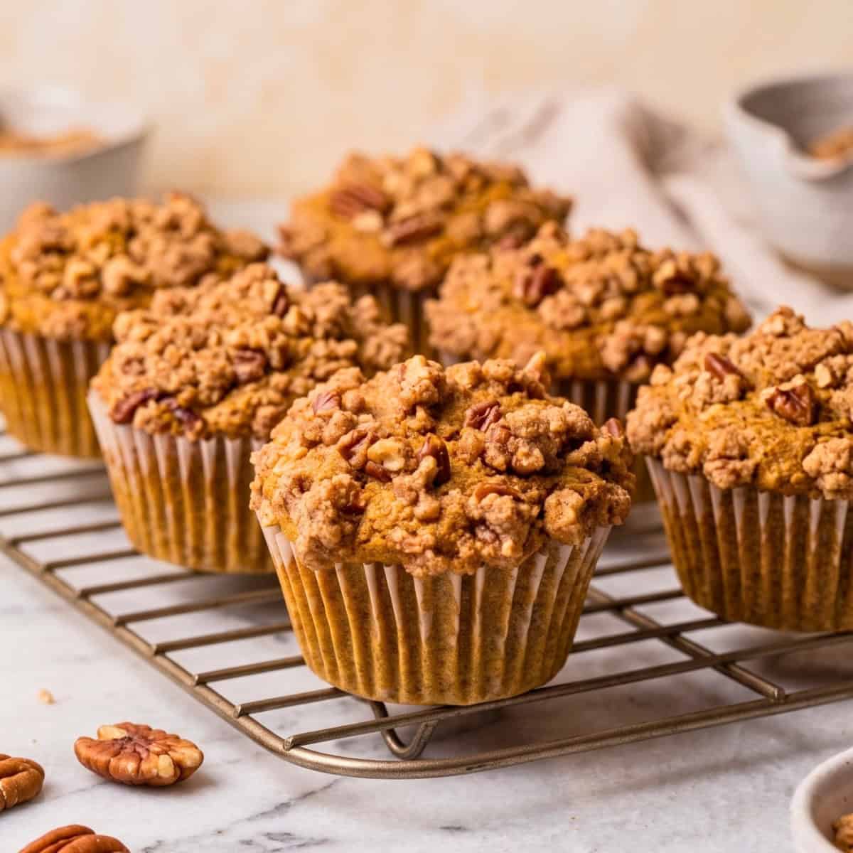 A batch of baked vegan pumpkin muffins with pecan streusel on a cooling rack.